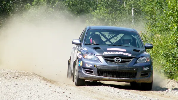 Voiture de rallye soulevant un nuage de poussière sur une piste en terre